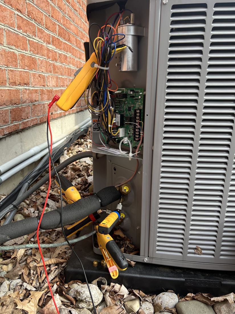 Refrigerant gauges and a multimeter connected to an open air conditioner control panel during a service call