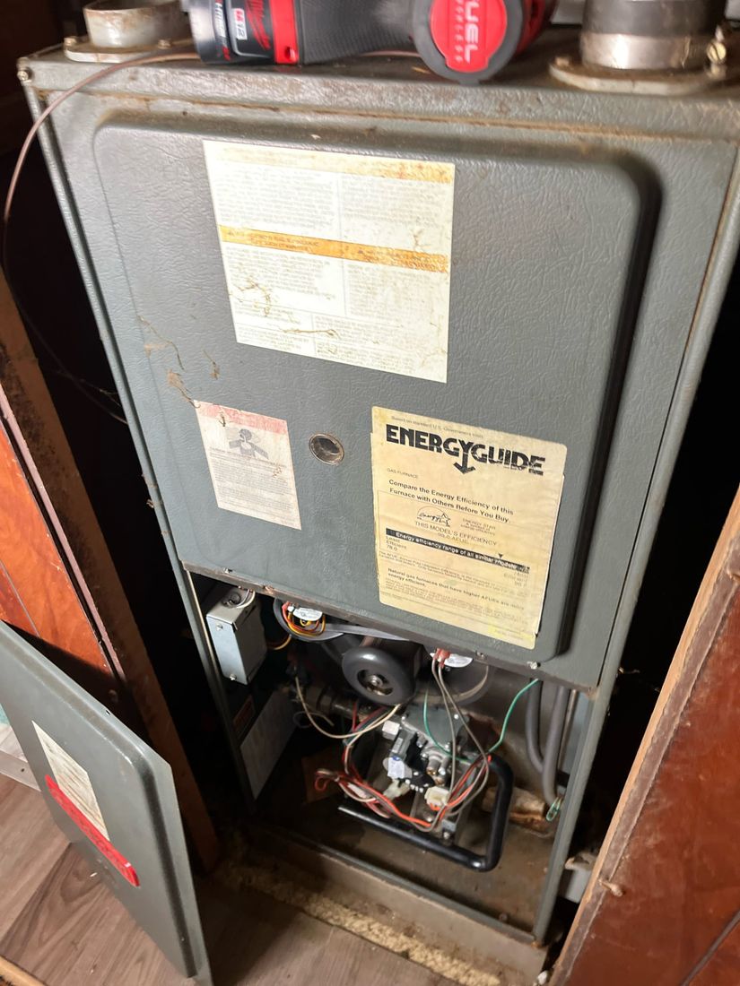 An older gas furnace opened up during a repair call, burner compartment and flame sensor exposed