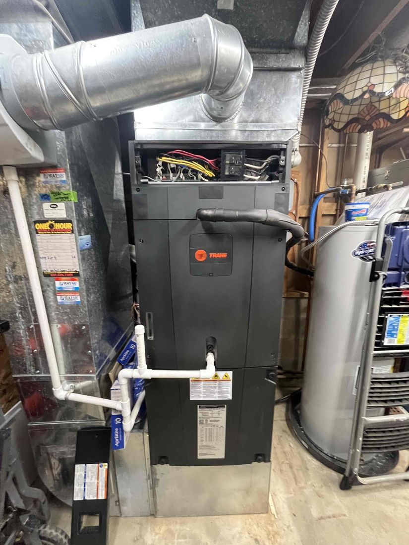 A Trane furnace in a basement with its control panel open for service